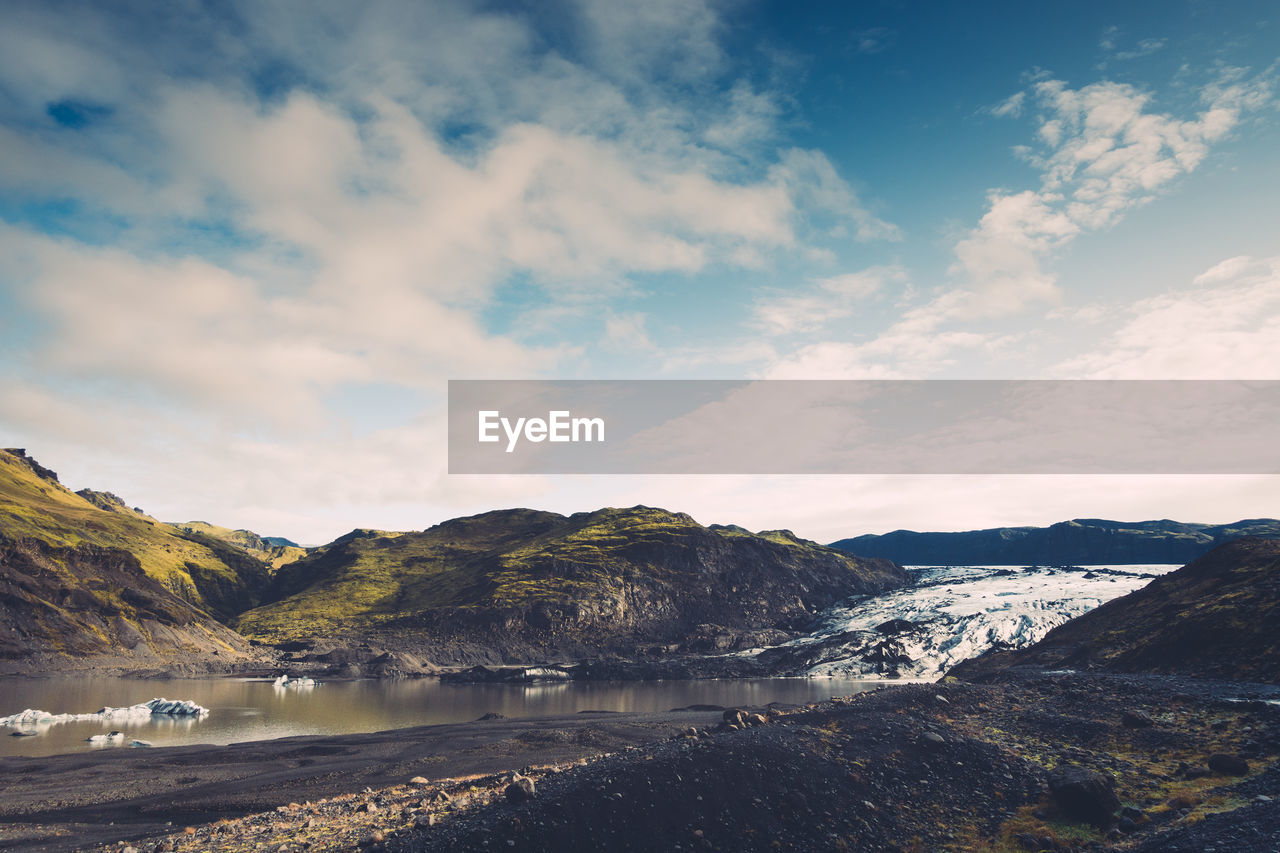 Scenic view of lake by mountains against cloudy sky