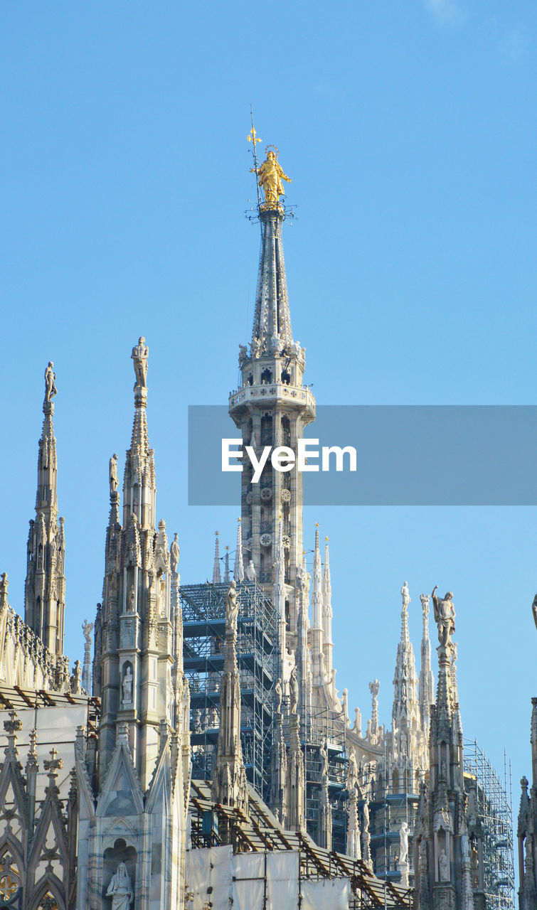 Low angle view of statue at milan cathedral against blue sky
