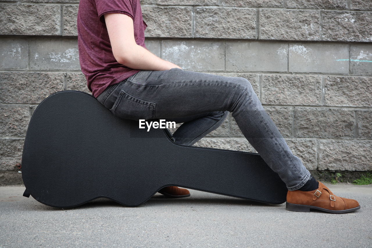 Low section of man sitting on guitar case against wall