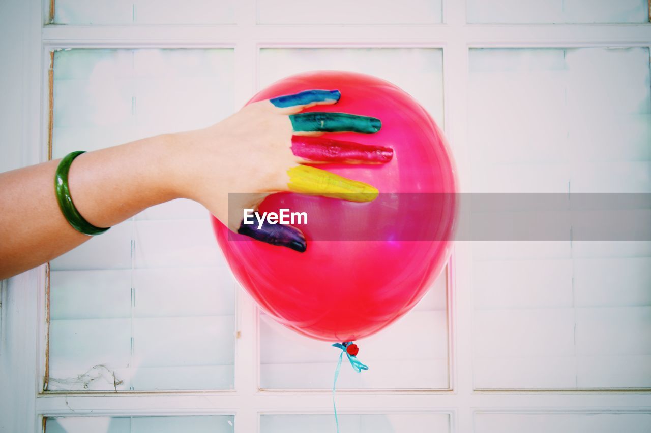Cropped colorful watercolor paints covered hand touching red helium balloon