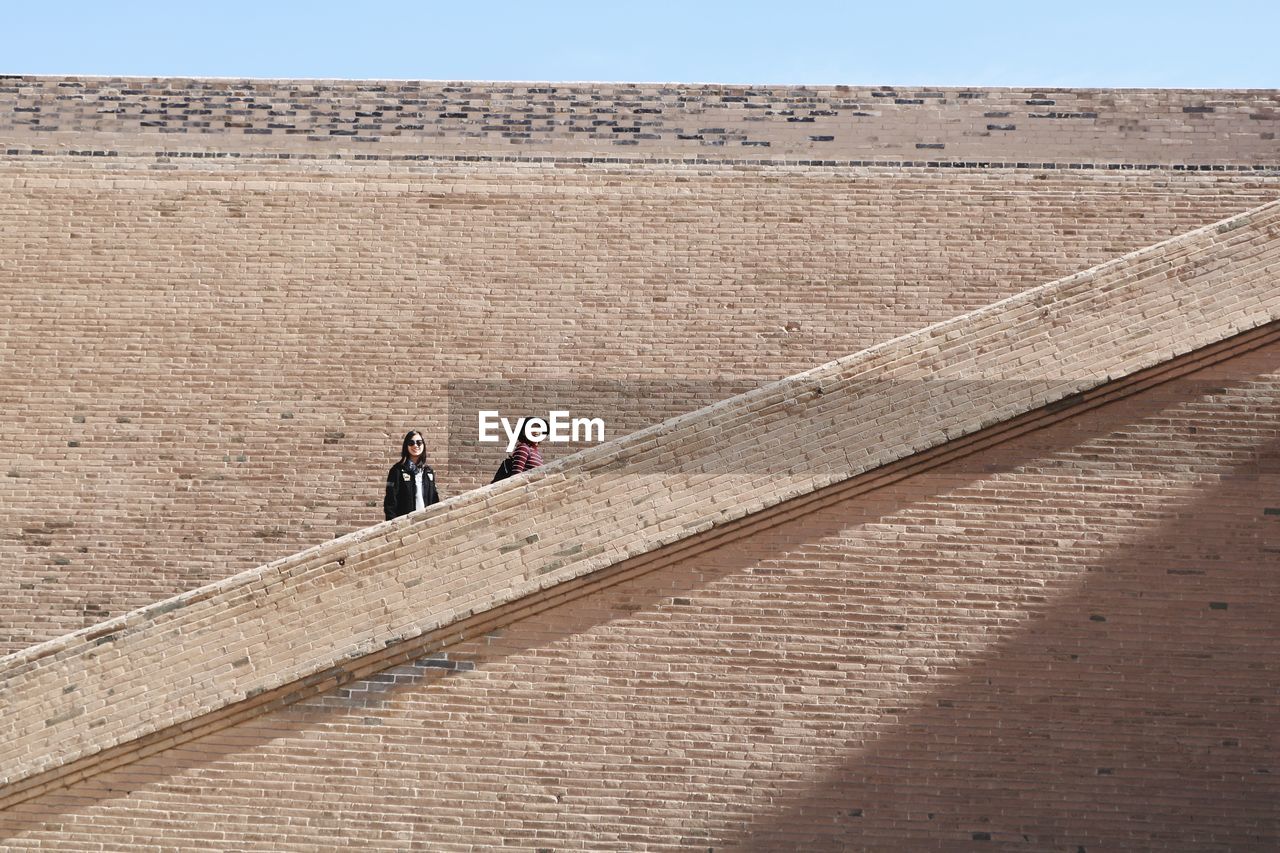 Low angle view of female friends on steps against wall