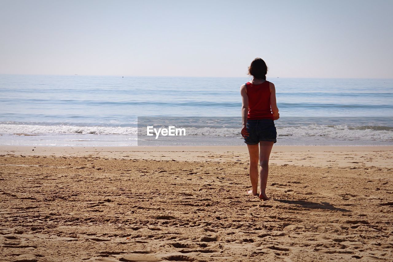 Rear view of woman standing at beach against sky