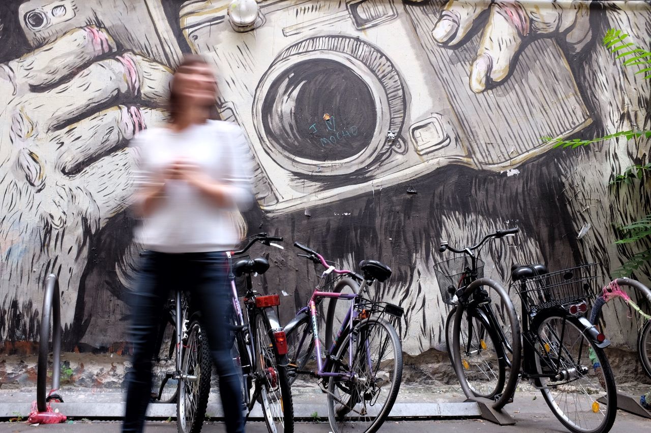 Blurred motion of woman standing by bicycles against graffiti wall