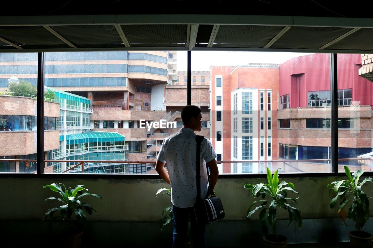 REAR VIEW OF MAN STANDING BY BUILDING