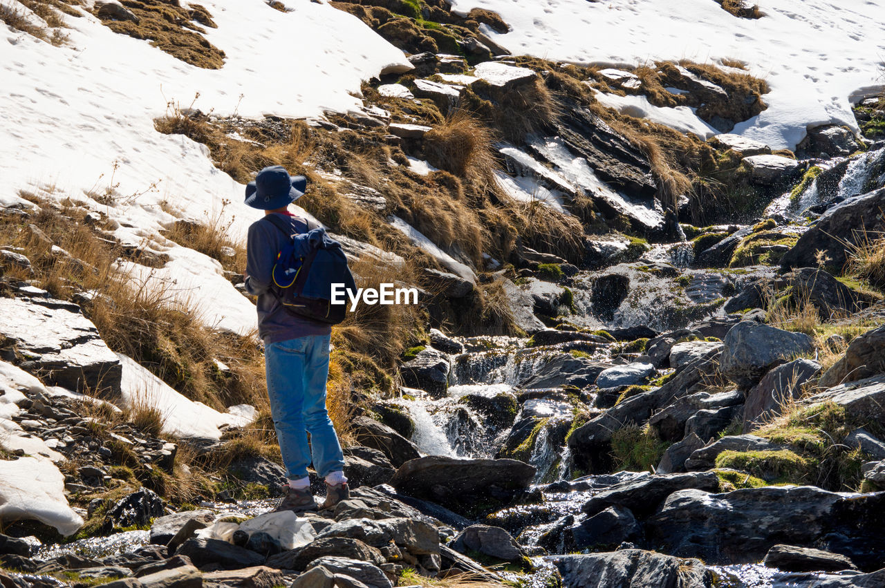 FULL LENGTH REAR VIEW OF MAN STANDING ON ROCKS