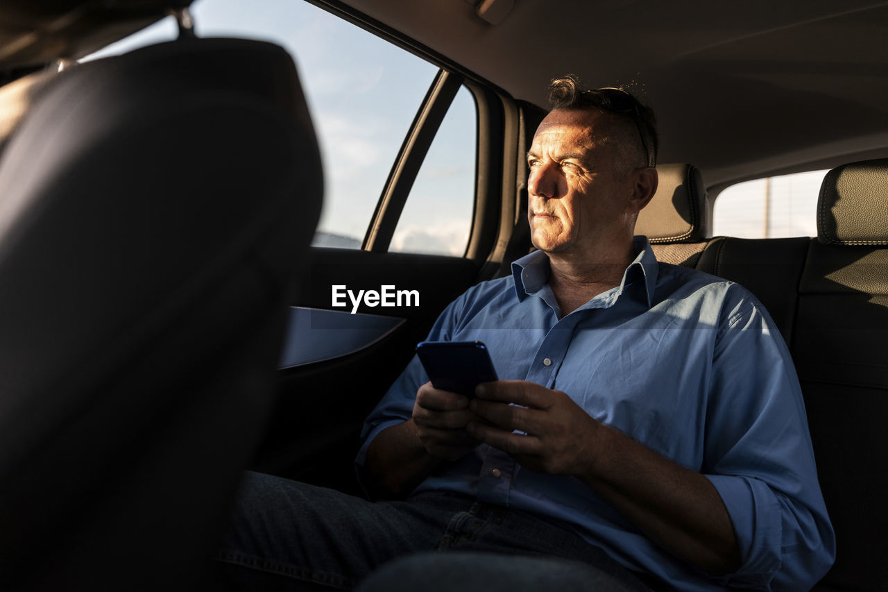 Mature male professional looking away while sitting with smart phone in car