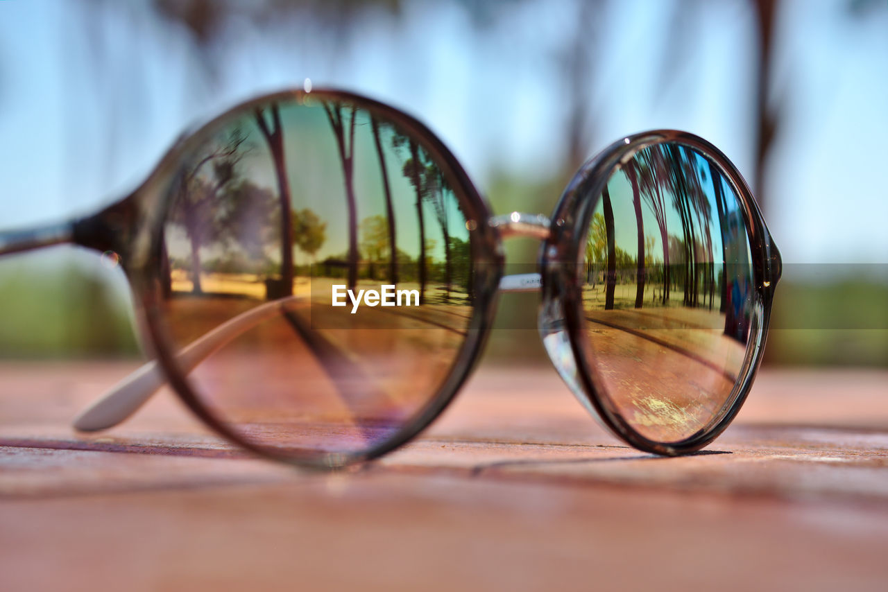 Close-up of sunglasses with trees reflecting on table
