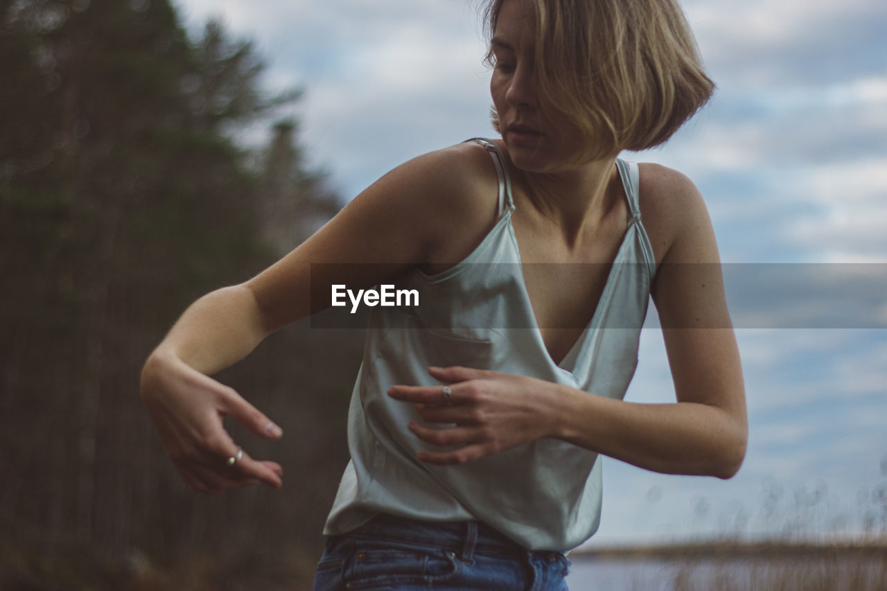 Close-up of beautiful woman dancing against cloudy sky