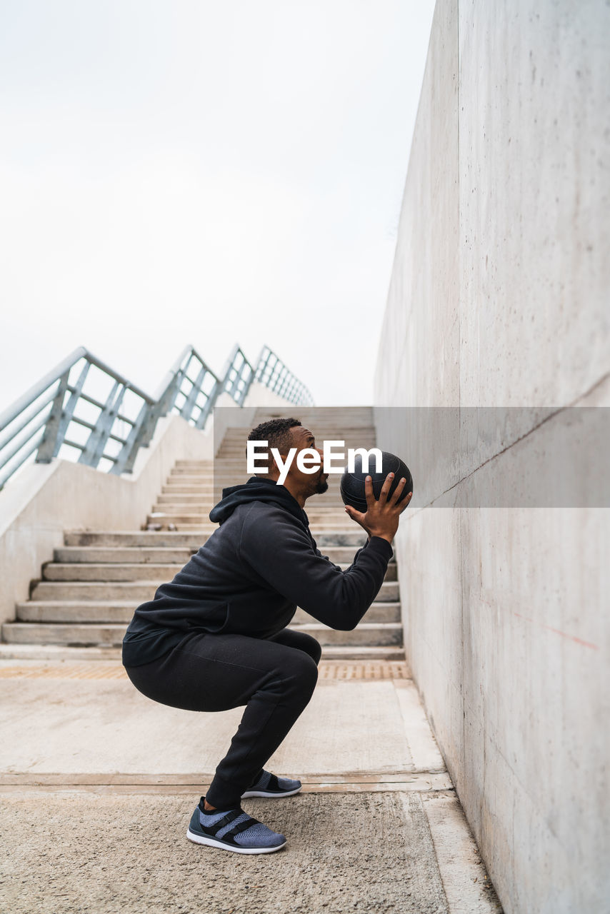 Full length of man exercising outdoors with medicine ball against wall