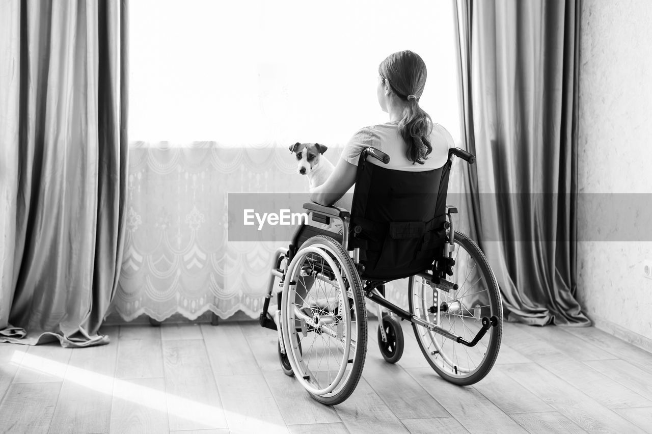 side view of woman using mobile phone while sitting on wheelchair at home