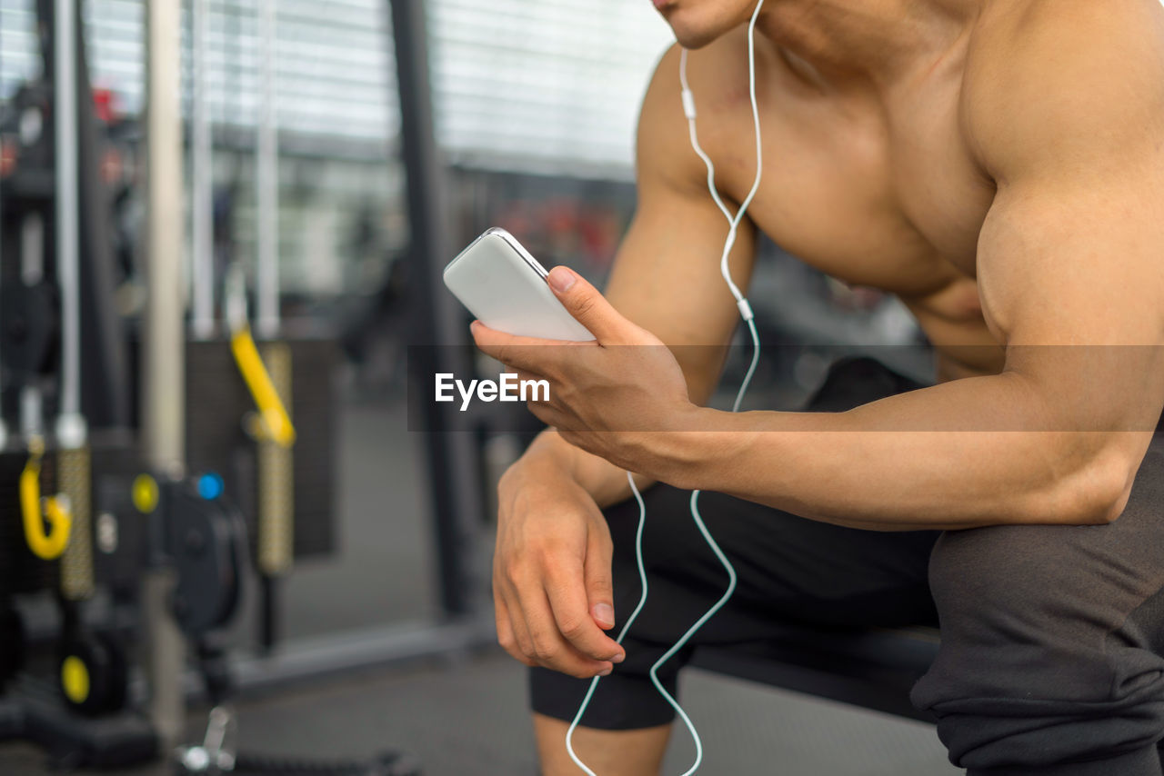 Midsection of shirtless muscular man using mobile phone in gym