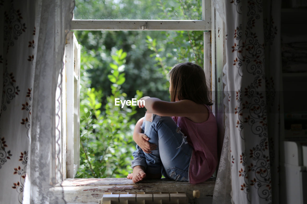 Child girl on the window, the concept of sadness and loneliness, the problems of childhood