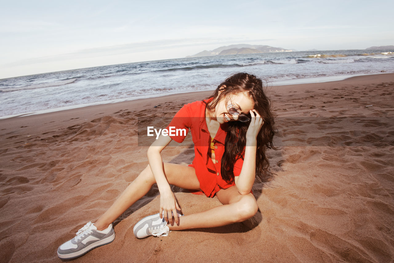 full length of young woman sitting on sand at beach