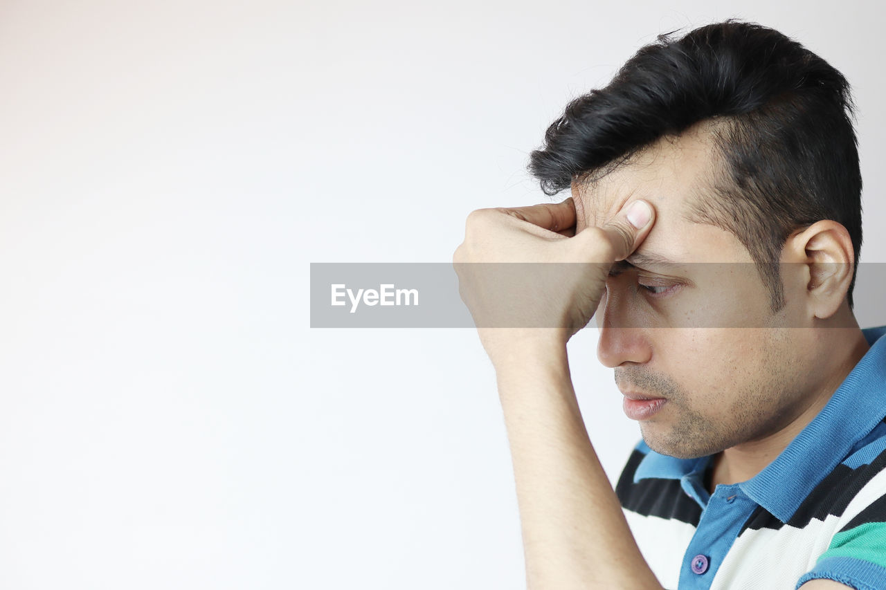 Close-up of man touching forehead in pain against white background