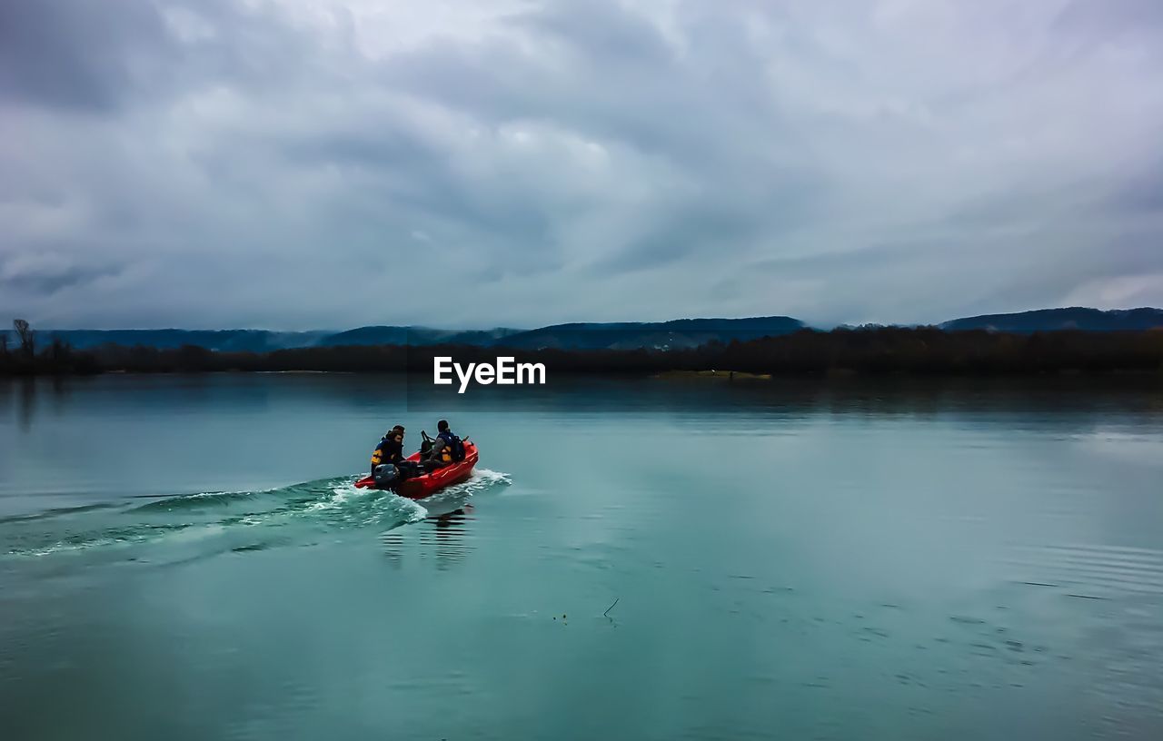 People sitting in boat on river against cloudy sky