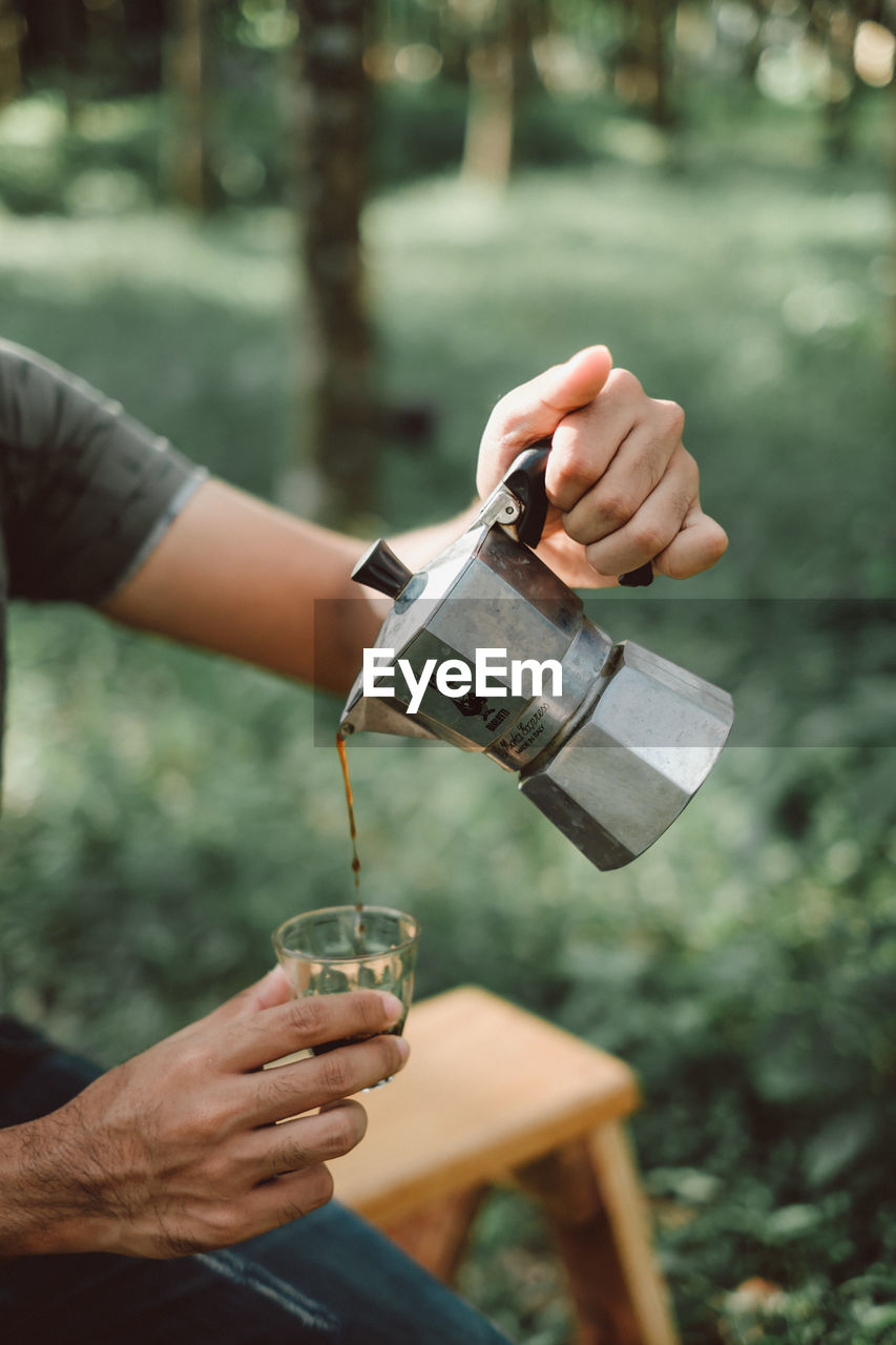 Midsection of man pouring coffee in glass on field