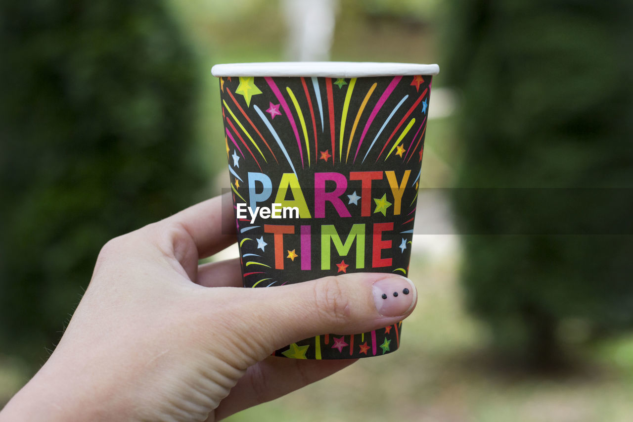 A hand of person holding multi colored paper coffee cup