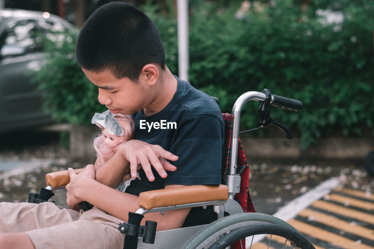 Boy holding doll sitting on wheelchair