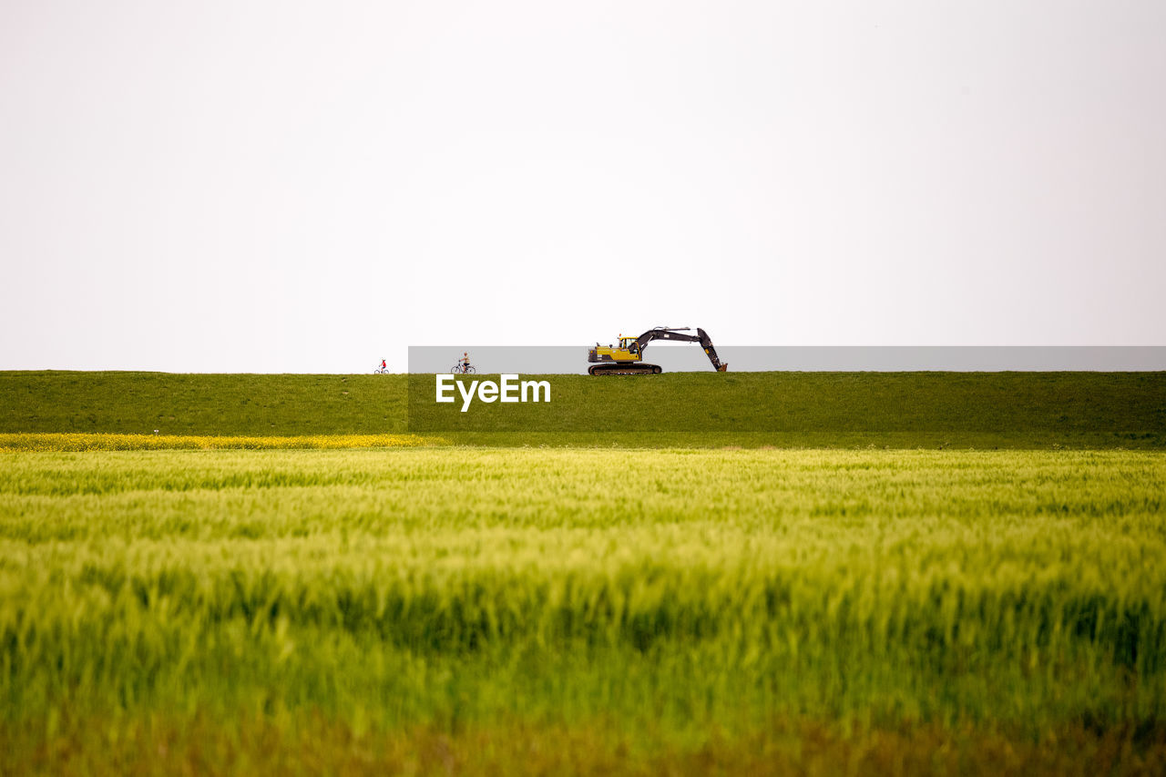 Excavator on grassy field against clear sky