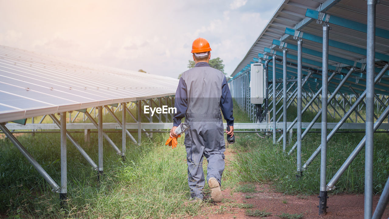 Engineer walking amidst at solar panel against sky