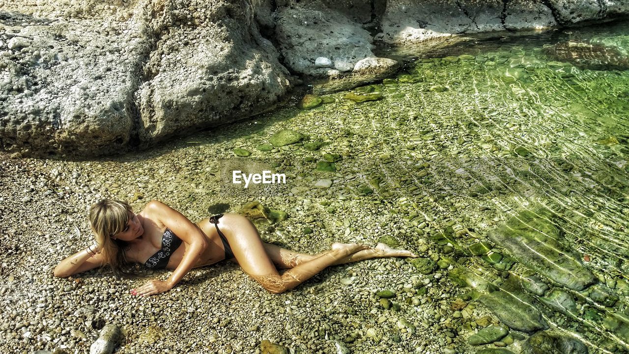 High angle view of sensuous woman in bikini lying on shore at beach