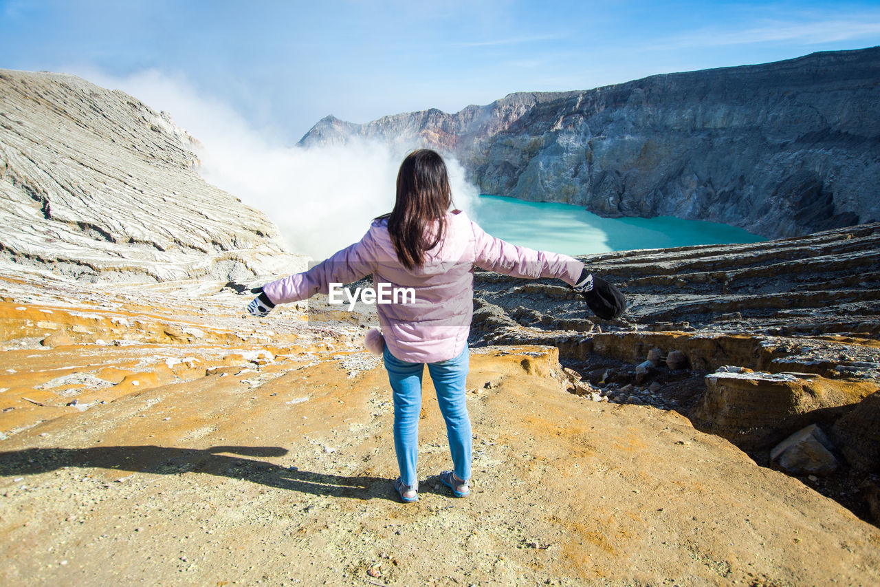 Rear view of woman with arms outstretched standing on rock 