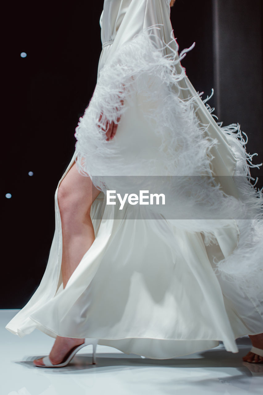 Elegant fashion details of white long silky bridal dress. fashion model walking on black background