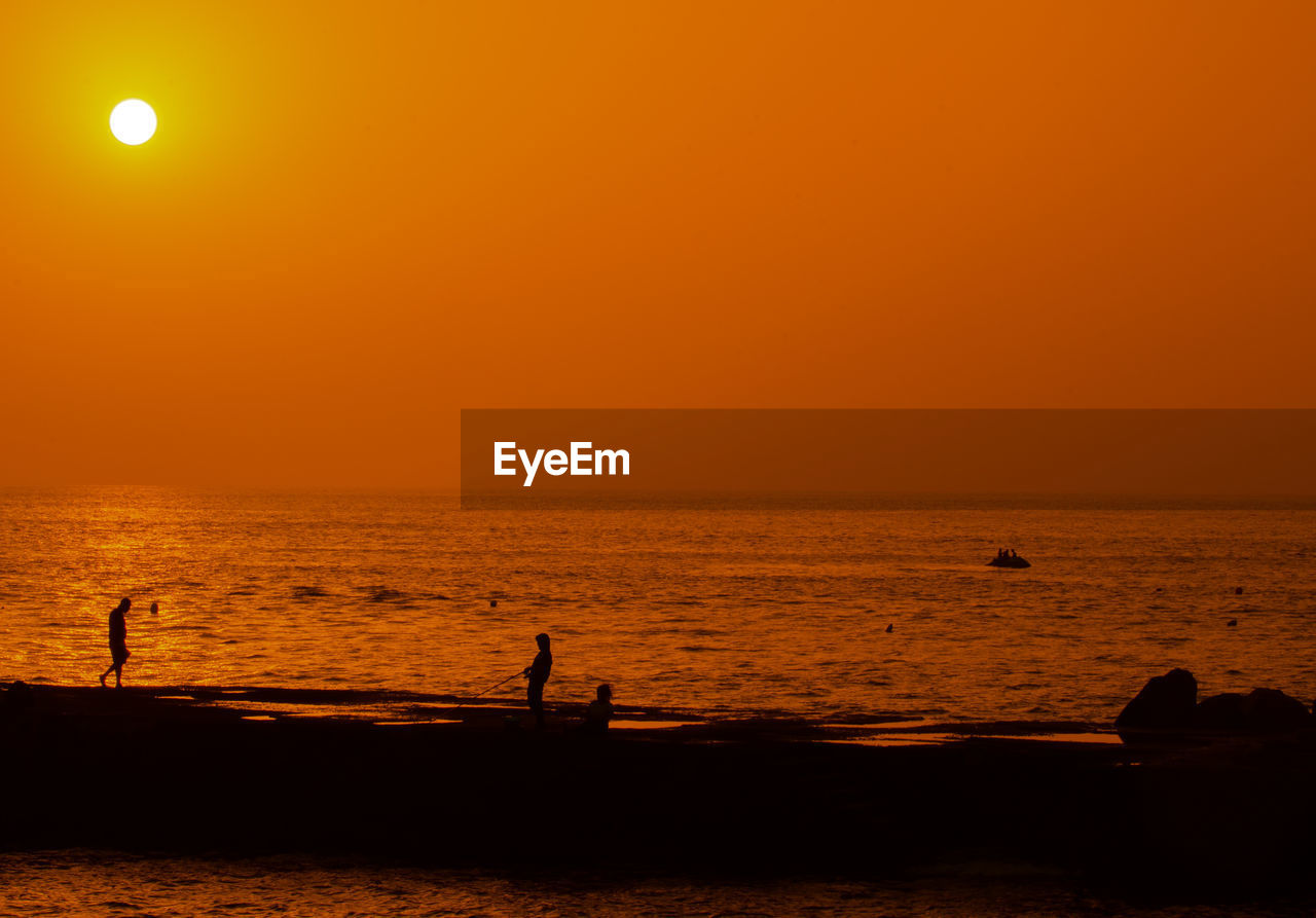 SILHOUETTE PEOPLE ON BEACH AGAINST ORANGE SKY