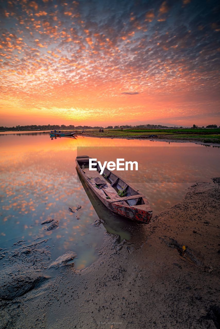 Boat moored on beach against sky during sunset