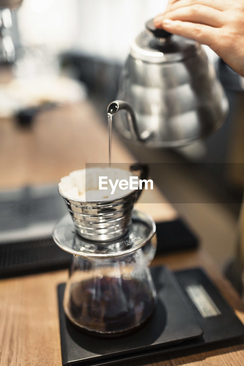 Cropped image of barista pouring boiling water in coffee filter at counter
