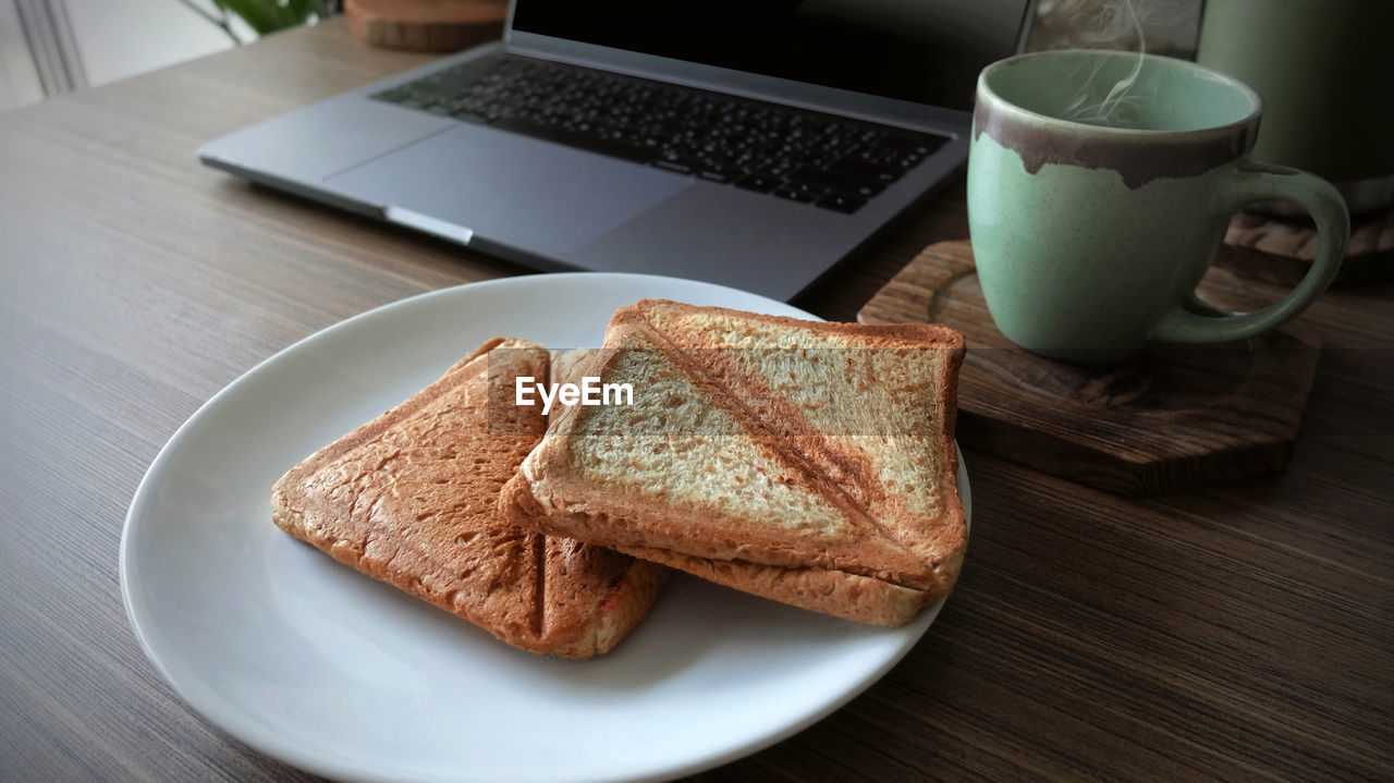 Closeup bun with coffee cup and laptop on wooden table, morning time, empty space for text