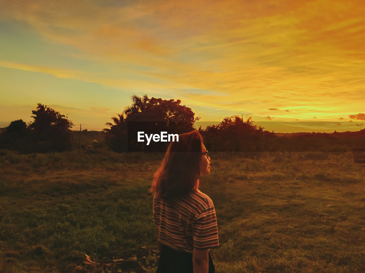 Woman standing on field against sky during sunset