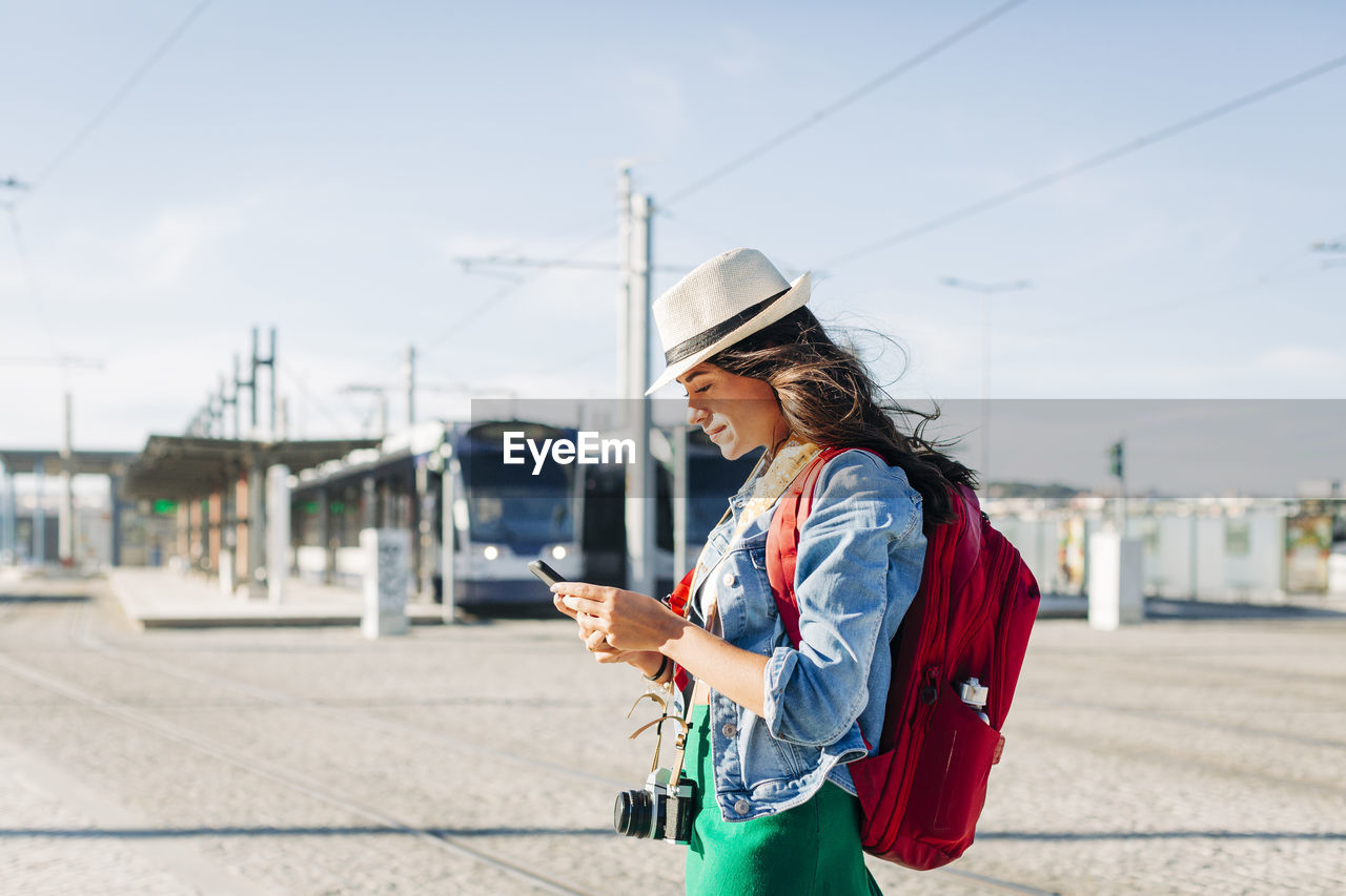 Smiling young woman wearing hat using smart phone on sunny day