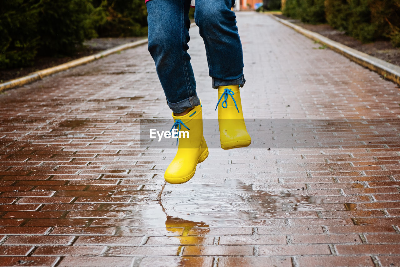 Jumping in puddle. female legs in yellow rubber boots jumping on the puddle. carefree young woman