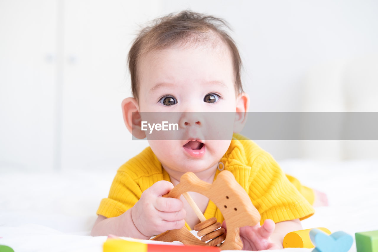 Healthy asian baby girl in yellow bodysuit playing with wooden toys on white bedding