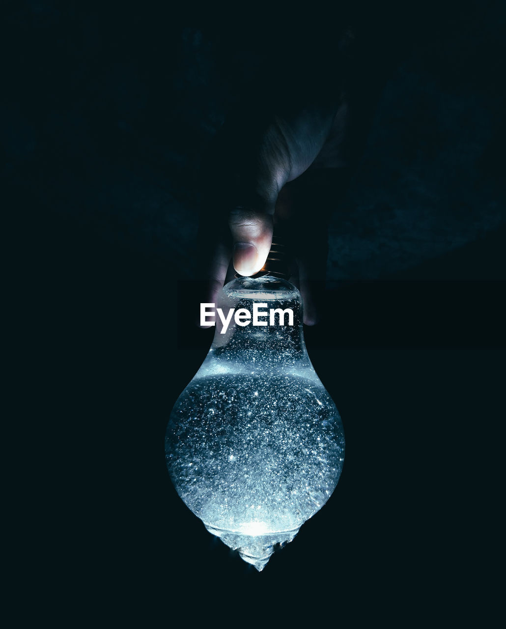 Close-up of hand holding illuminated light bulb in dark