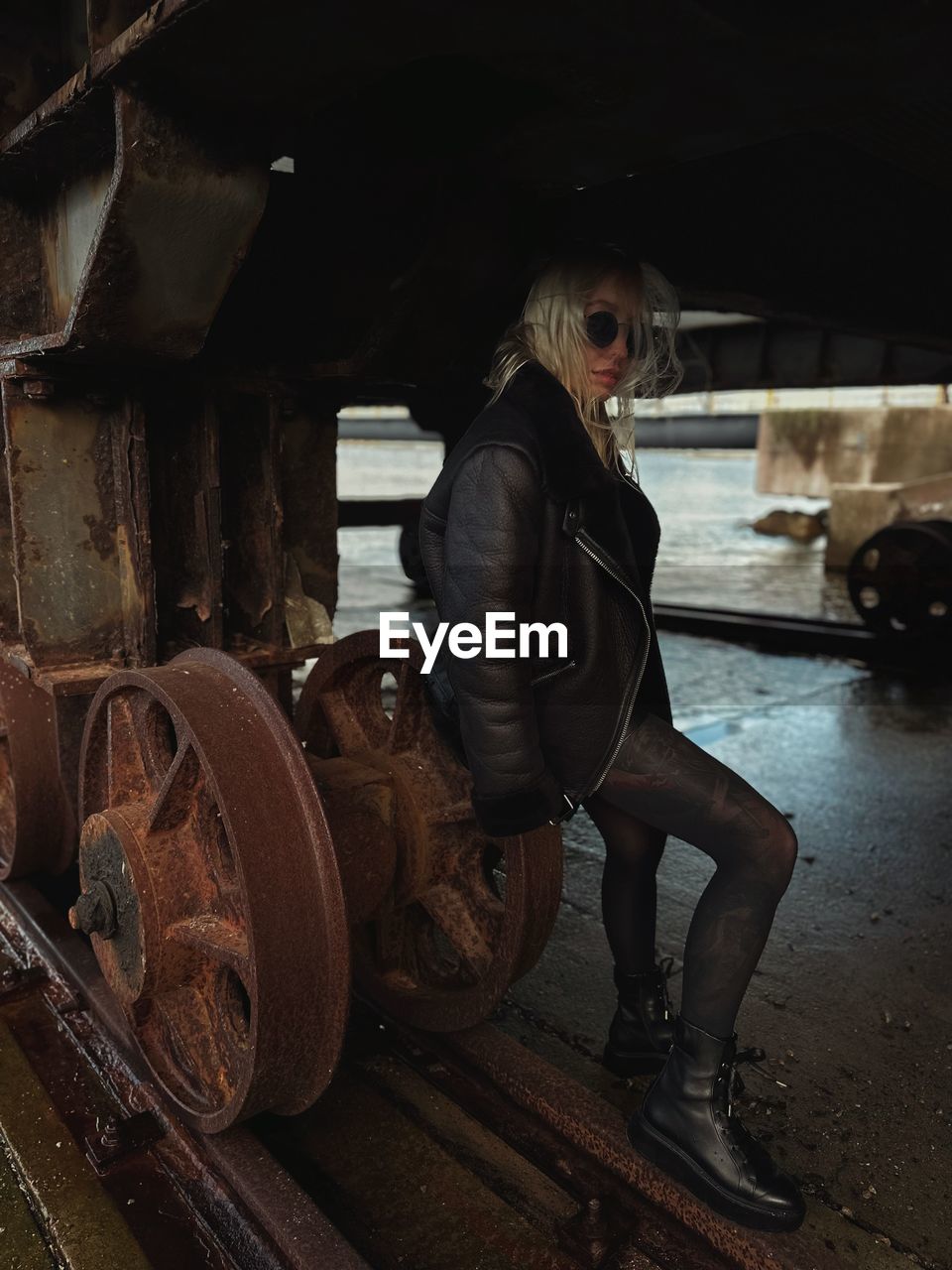 one person, adult, transportation, mode of transportation, darkness, wheel, tire, full length, clothing, standing, indoors, women, architecture, screenshot, business, person, barrel, occupation, vehicle, young adult, portrait