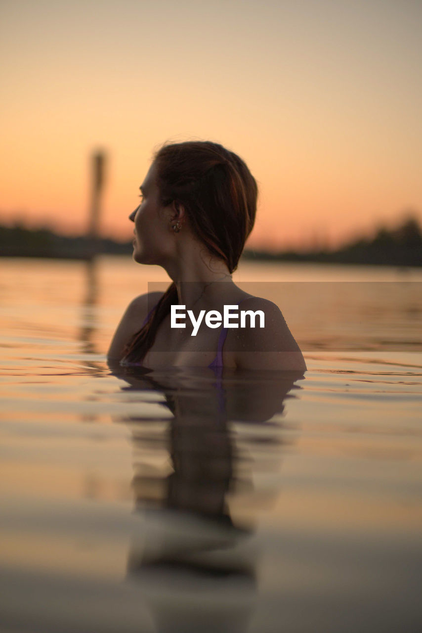 side view of young man swimming in sea against sky during sunset