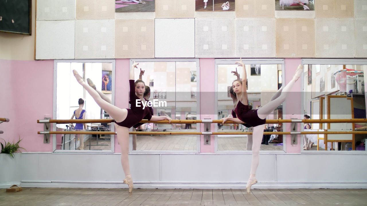 In dancing hall, young ballerinas in purple leotards perform grand battement back on pointe shoes