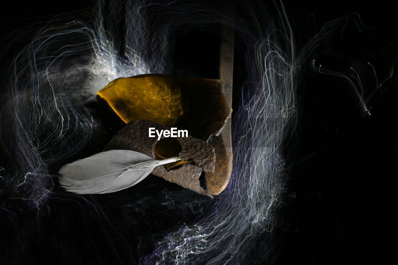 Close-up of rusty metal with feather over light painting against black background