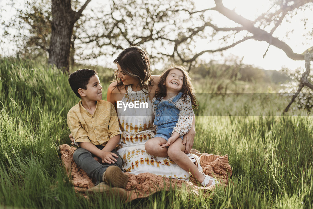 Mother, son, and daughter in backlit field smiling at each other