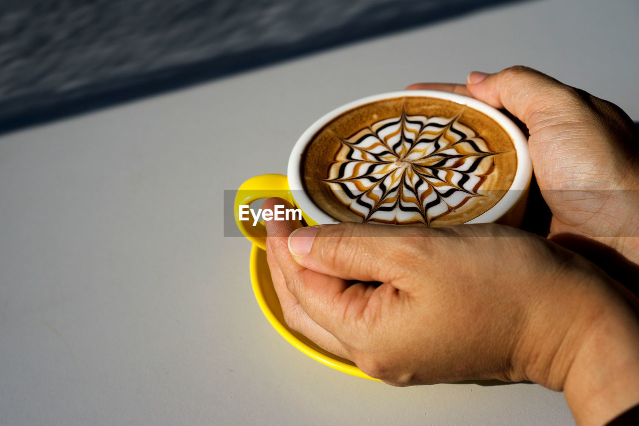 Hand holding a yellow cup of latte coffee