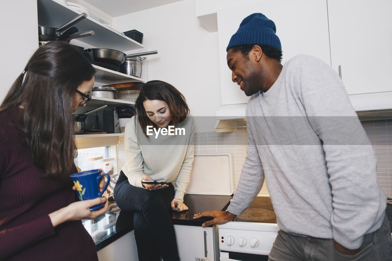 Young woman showing mobile phone to roommates in kitchen