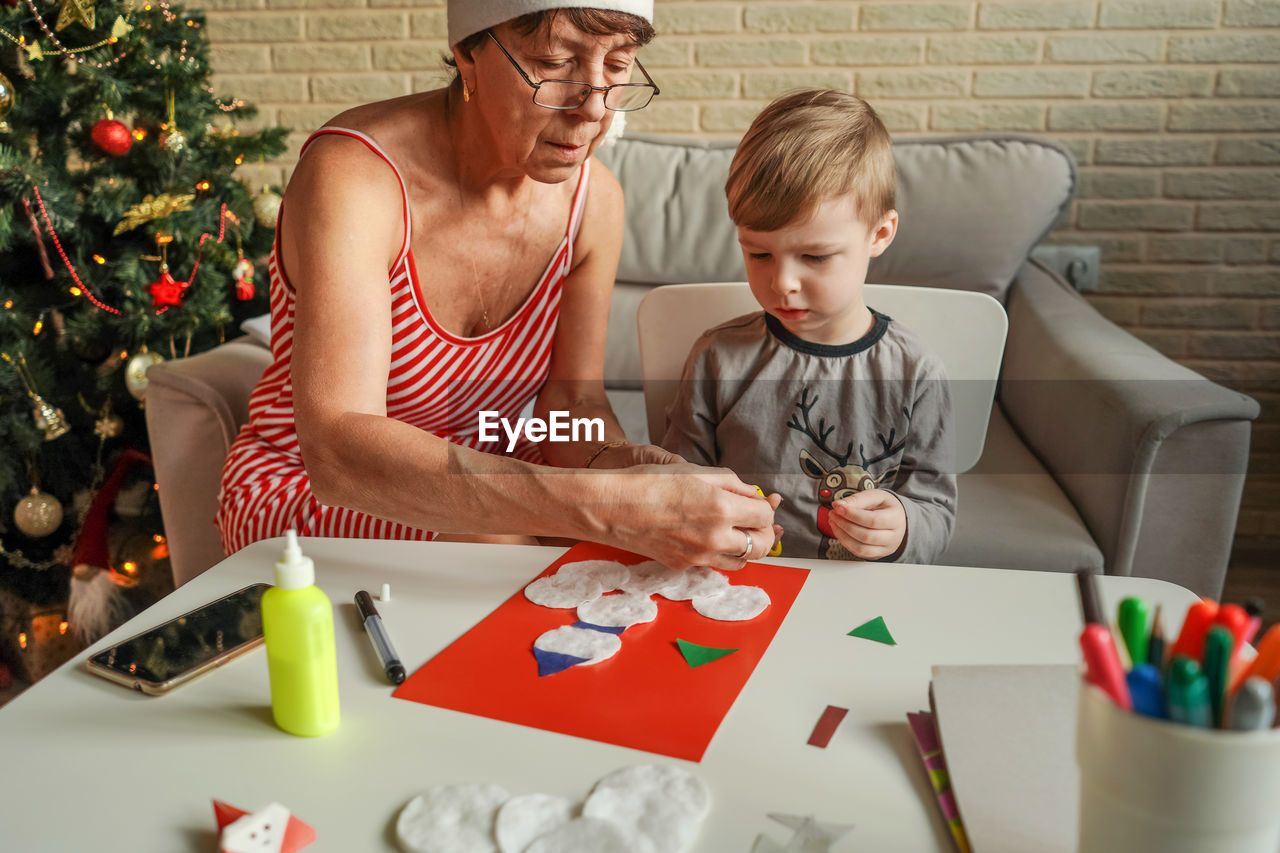 Senior woman with grandson making greeting card on table at home