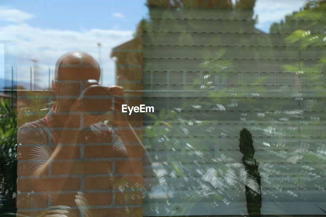 Reflection of man photographing on glass