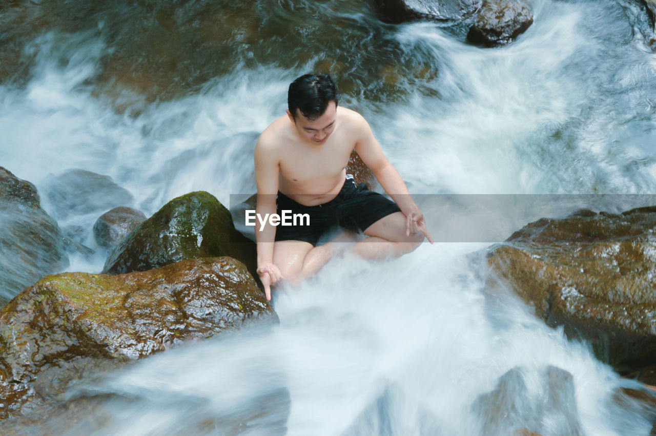 High angle view of man meditating in waterfall
