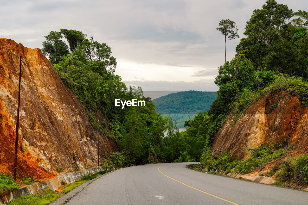 Road amidst trees and mountains against sky