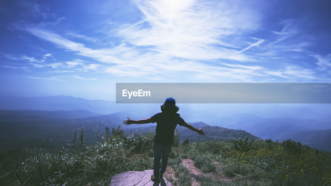 rear view of man jumping on mountain against sky