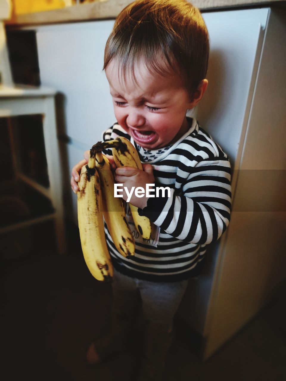 Cute girl with banana crying while standing in kitchen