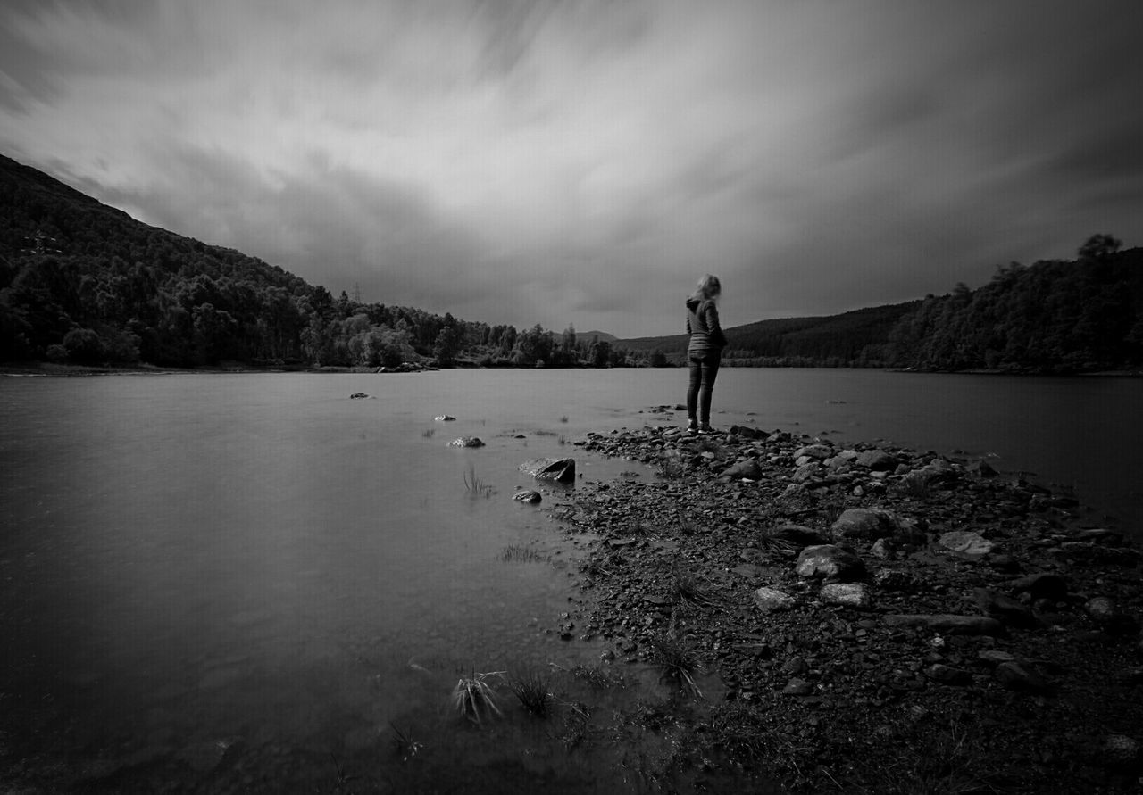 Side view of woman standing by lake against cloudy sky